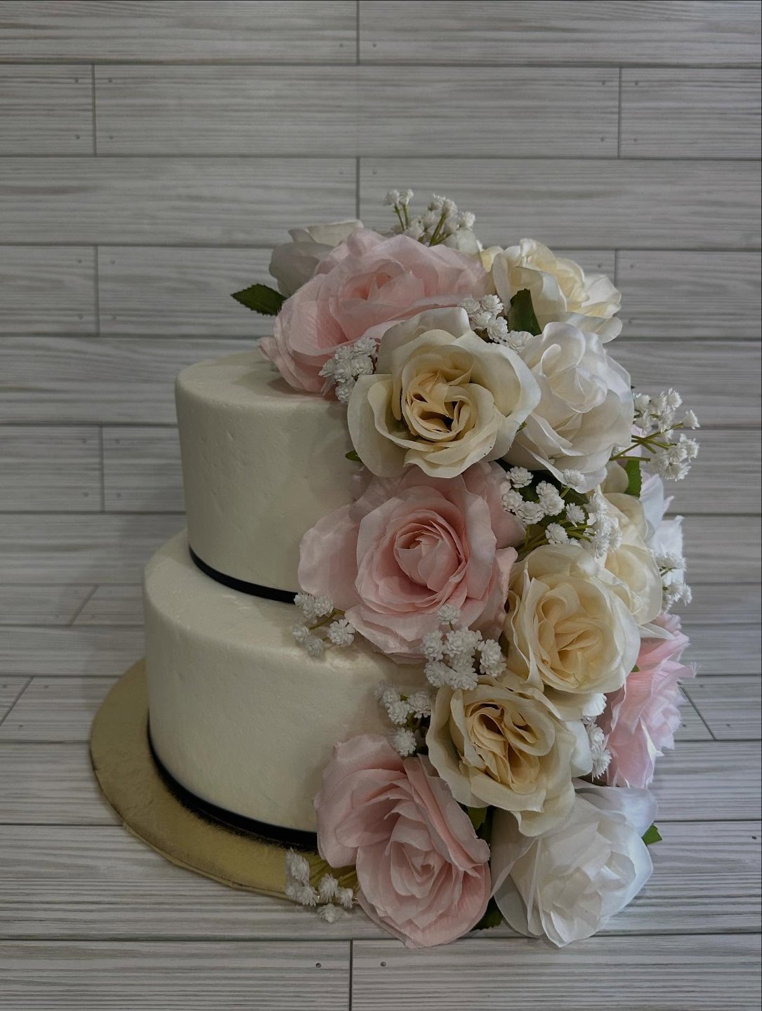 Two-tier white wedding cake with a black ribbon base and a cascade of blush and ivory roses
